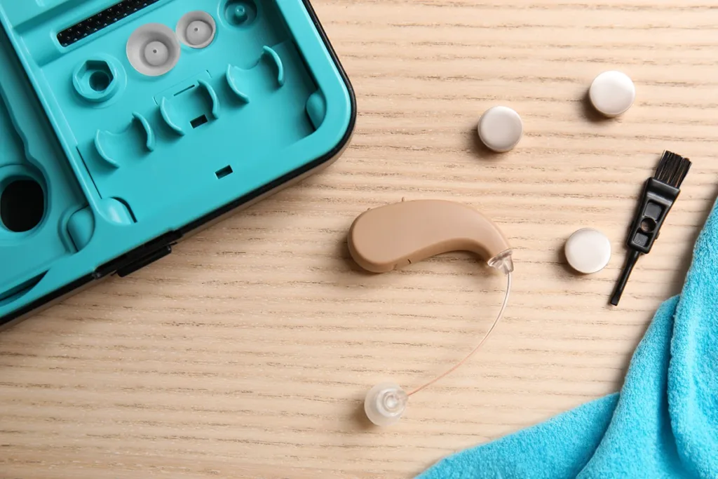 An above view of a BTE hearing aid and hearing aid cleaning supplies layout on a table, demonstrating the concept of how to properly clean your hearing aids at home.